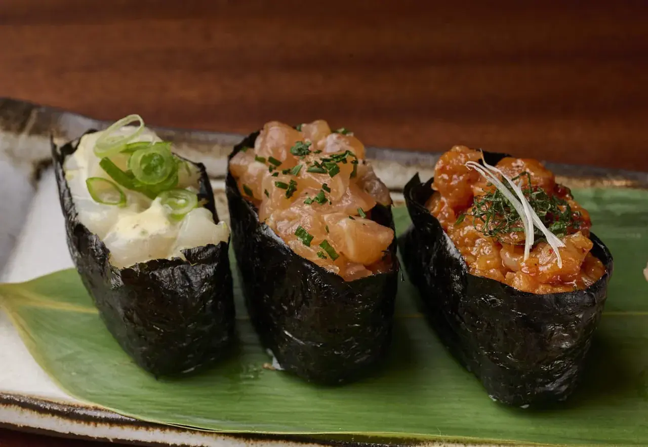 Drei leckere Sushi Gunkan mit Lachs, Garnelen und Fisch, garniert mit Frühlingszwiebeln und Kräutern.