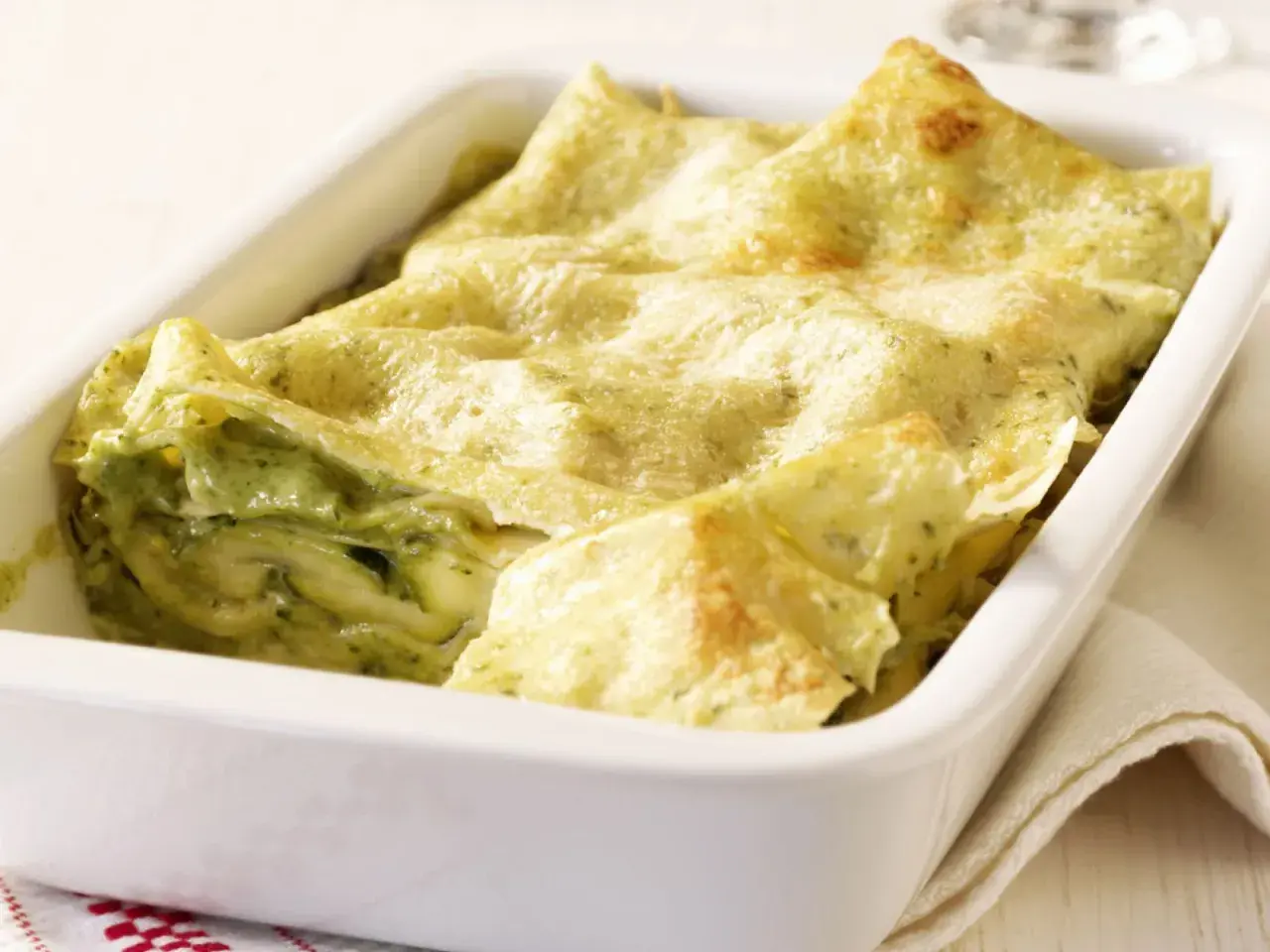 Zucchini-Lasagne mit cremiger Füllung und goldbraunen lasagneplatten in einer weißen Auflaufform.