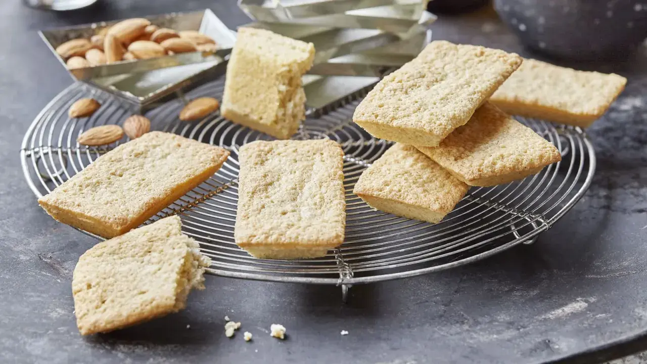 Goldbraune Financiers, frisch aus dem Ofen, warten auf das Financier Rezept. Mandeln liegen daneben.