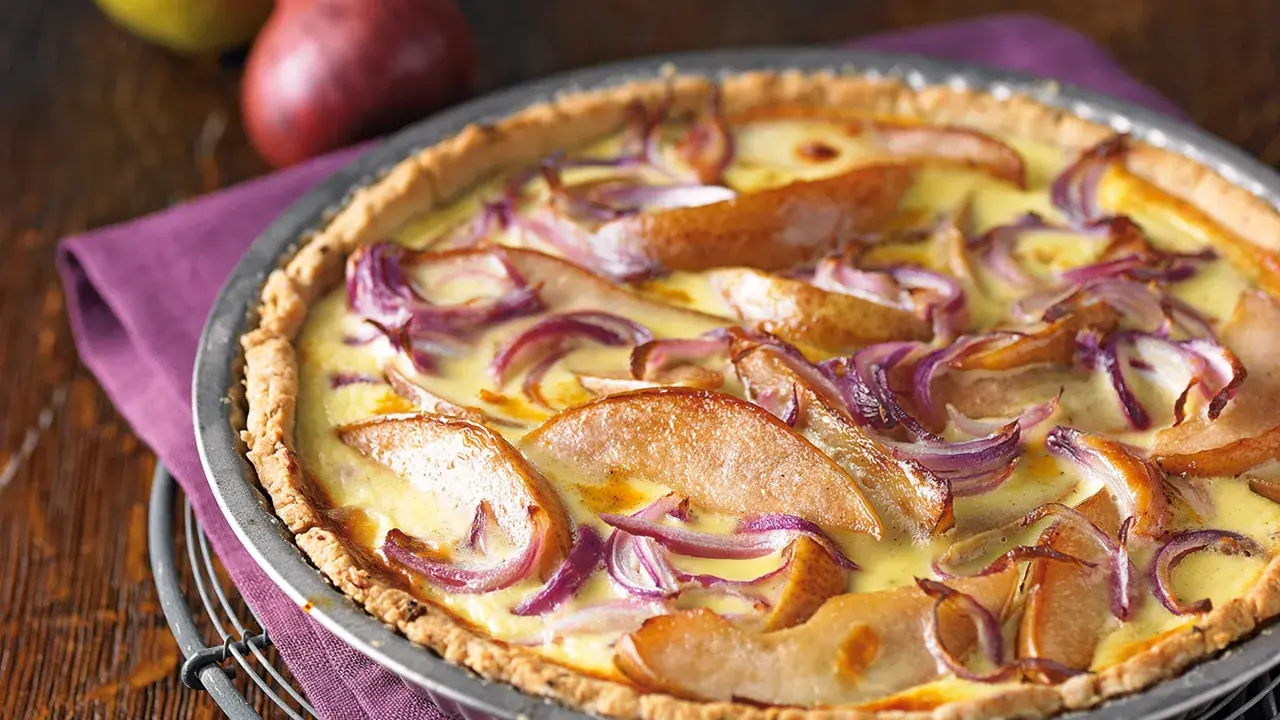 Herzhafte birnen quiche mit roten Zwiebeln und cremigem Guss, appetitlich in einer Metallform serviert.