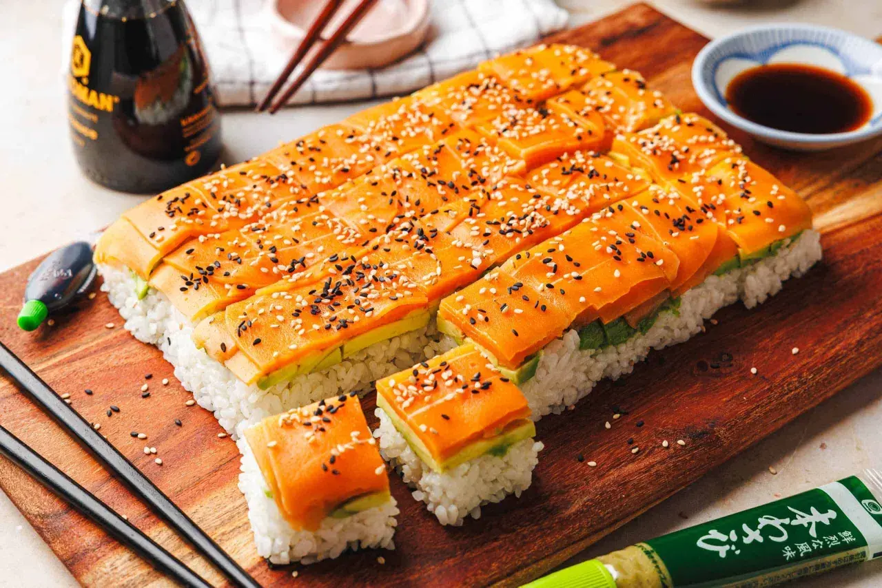 Leckere Sushi-Ideen: Reis, Avocado und Lachs, bestreut mit Sesam. Serviert auf einem Holzbrett mit Sojasauce und Wasabi.