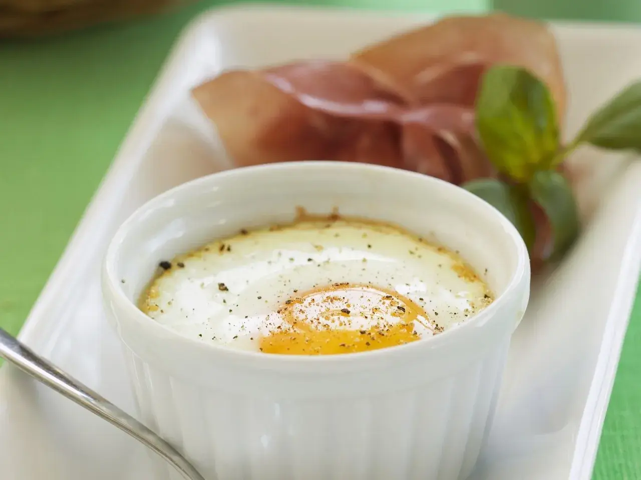 Ein köstliches oeuf cocotte mit einem perfekt gebratenen Ei, bestreut mit Pfeffer, serviert mit Schinken und Basilikum.
