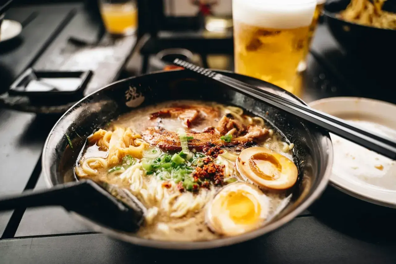 Herzhaftes Shoyu Ramen mit zartem Schweinefleisch, perfekt gekochtem Ei und Frühlingszwiebeln. Daneben ein kühles Bier.