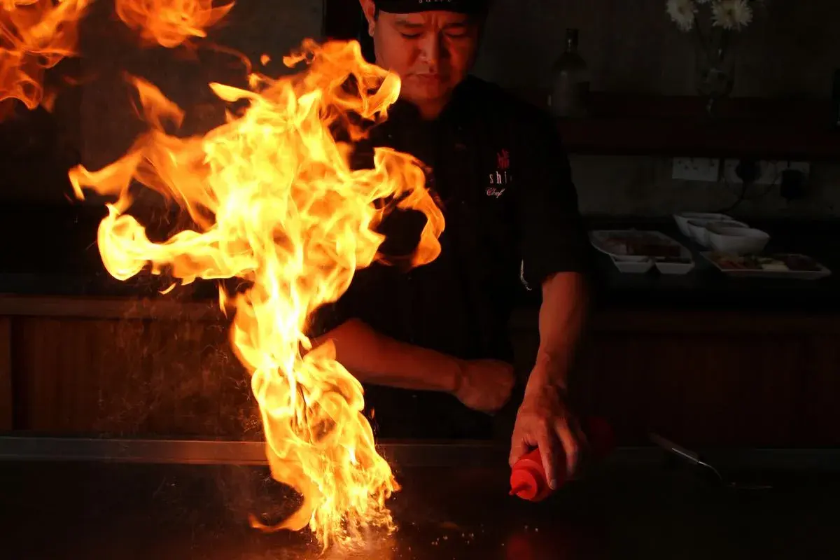 Ein Koch inszeniert mit flammendem Spektakel, was ist Teppanyaki: eine Showküche mit Feuer und Sauce.