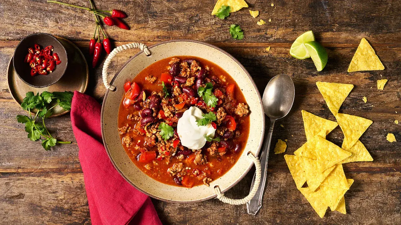 Herzhaftes Chili con Carne mit Bohnen, Hackfleisch und einem Klecks Sauerrahm, serviert mit Tortilla-Chips und Limette.