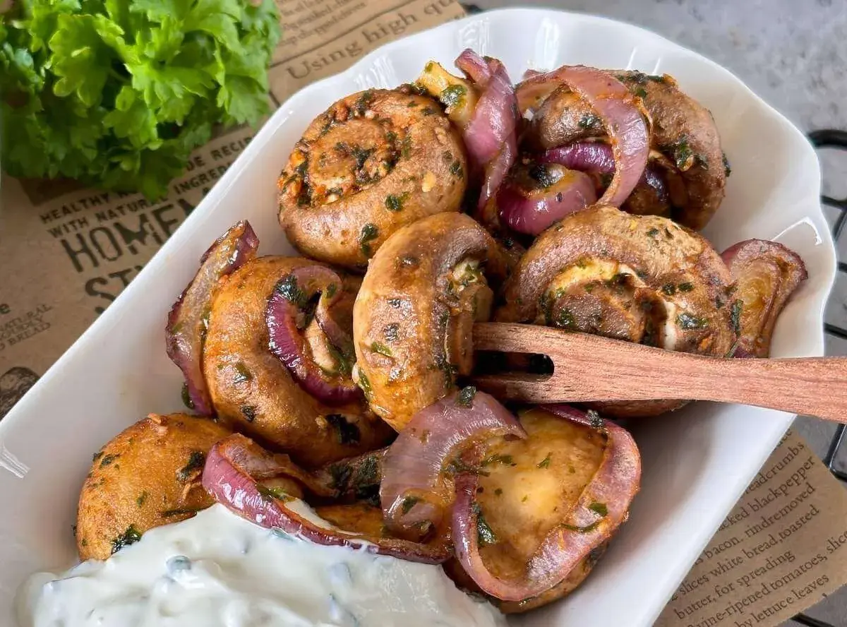 Gefüllte champignons aus dem airfryer mit roten Zwiebeln und Kräutern, serviert mit Dip.