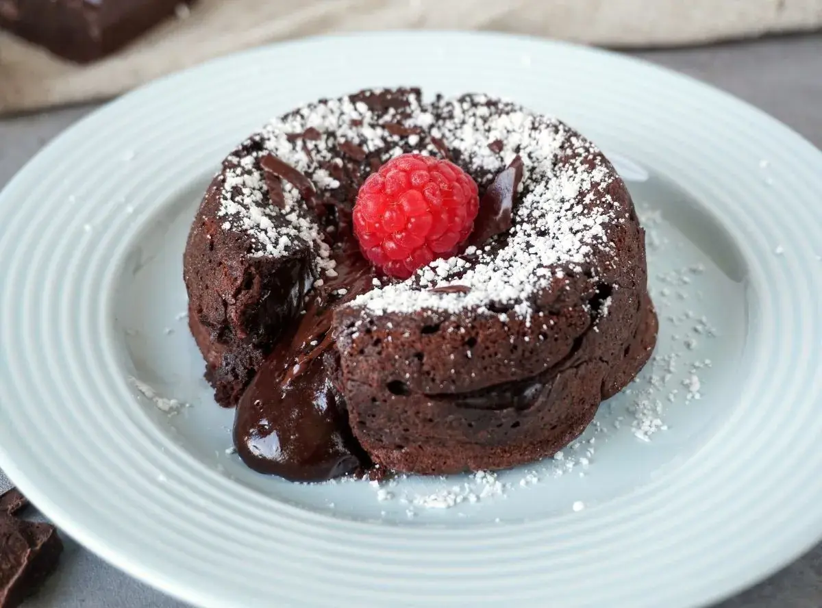 Schokokuchen mit weichem Kern, bestäubt mit Puderzucker und garniert mit einer Himbeere. Der flüssige Kern läuft verführerisch heraus.