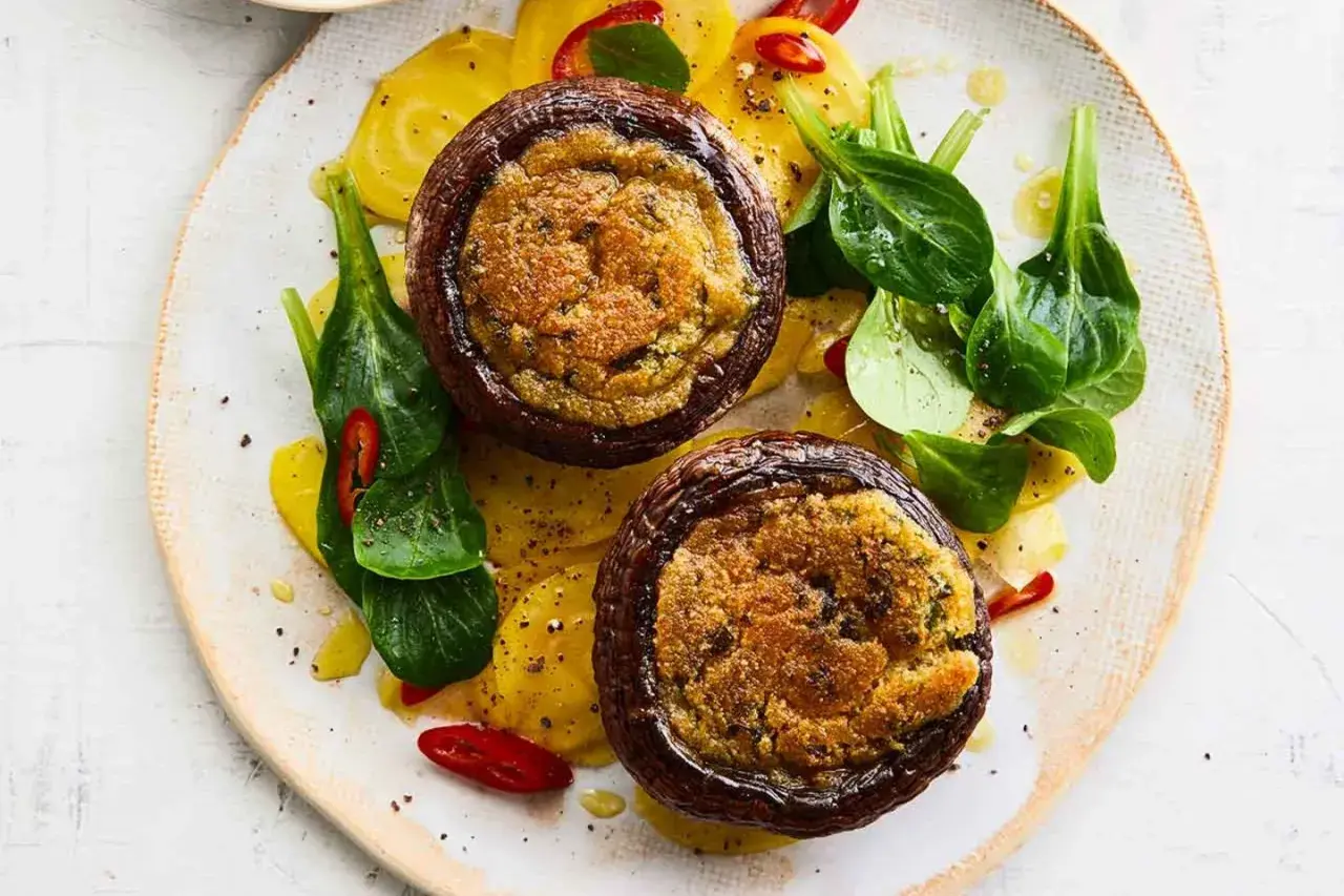 Zwei gefüllte Portobello Pilze auf gelben Ringen, garniert mit frischem Grün und Chilischeiben.