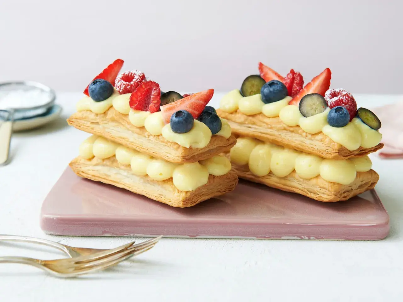 Zwei Mille-feuille-Törtchen mit Vanillecreme und frischen Beeren, bereit zum Genießen.