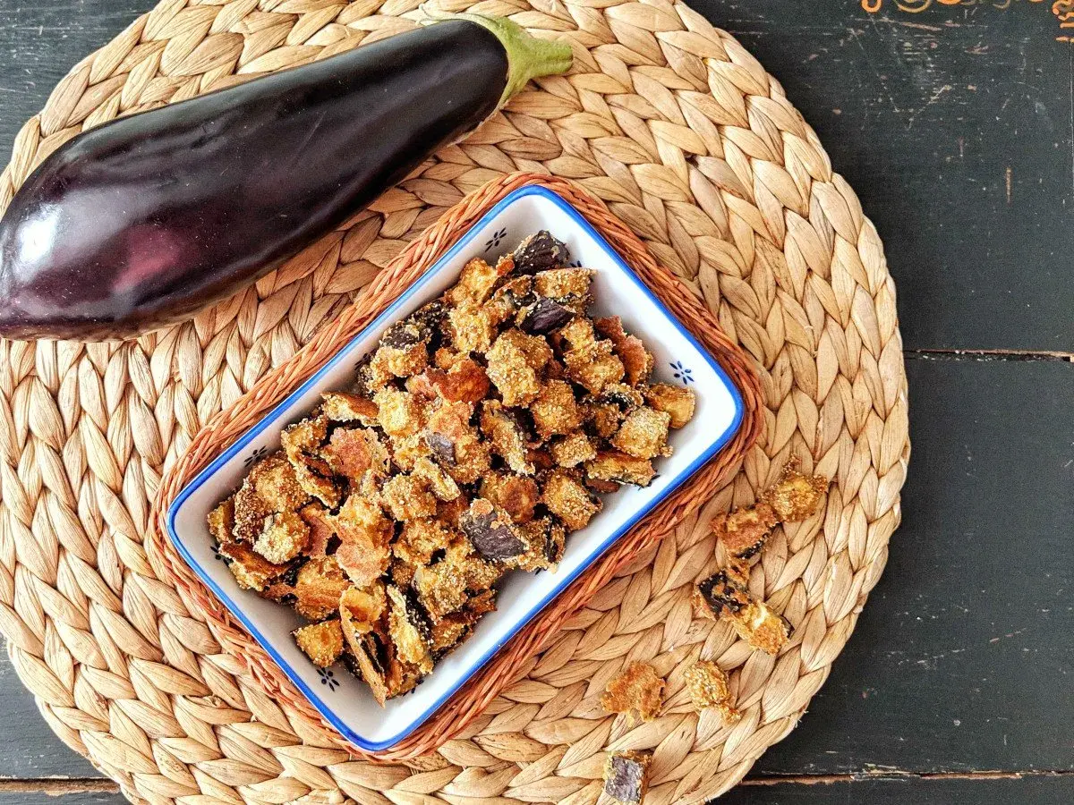 Knusprige, frittierte Aubergine in einer Schale, daneben eine ganze Aubergine. Ein leckerer Snack!