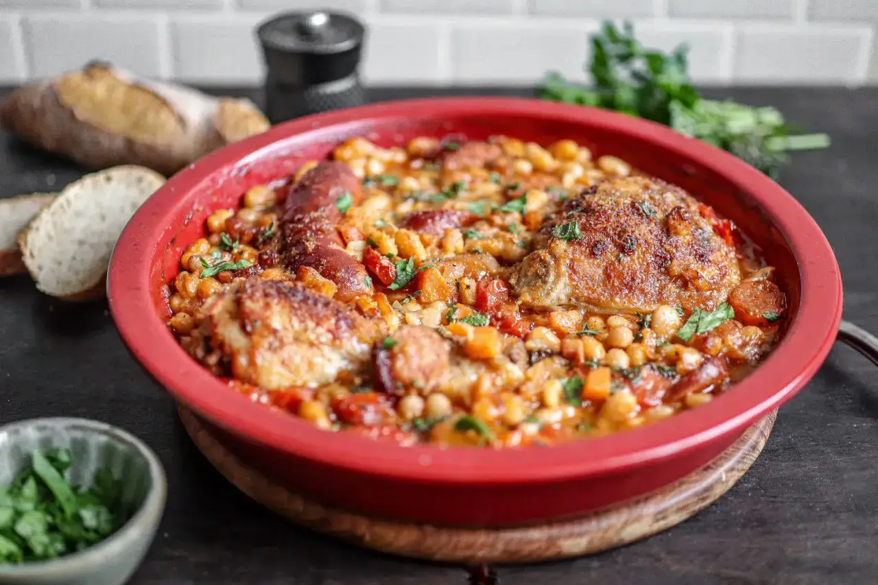 Herzhaftes Cassoulet Rezept in roter Auflaufform mit Hähnchen, Wurst und weißen Bohnen, garniert mit Petersilie.