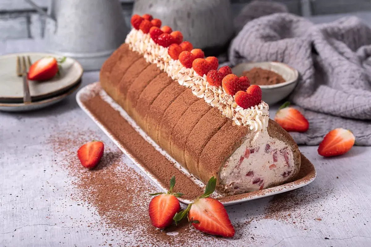 Erdbeer Tiramisu Rolle mit frischen Erdbeeren und Kakao bestäubt, ein Genuss für Augen und Gaumen.