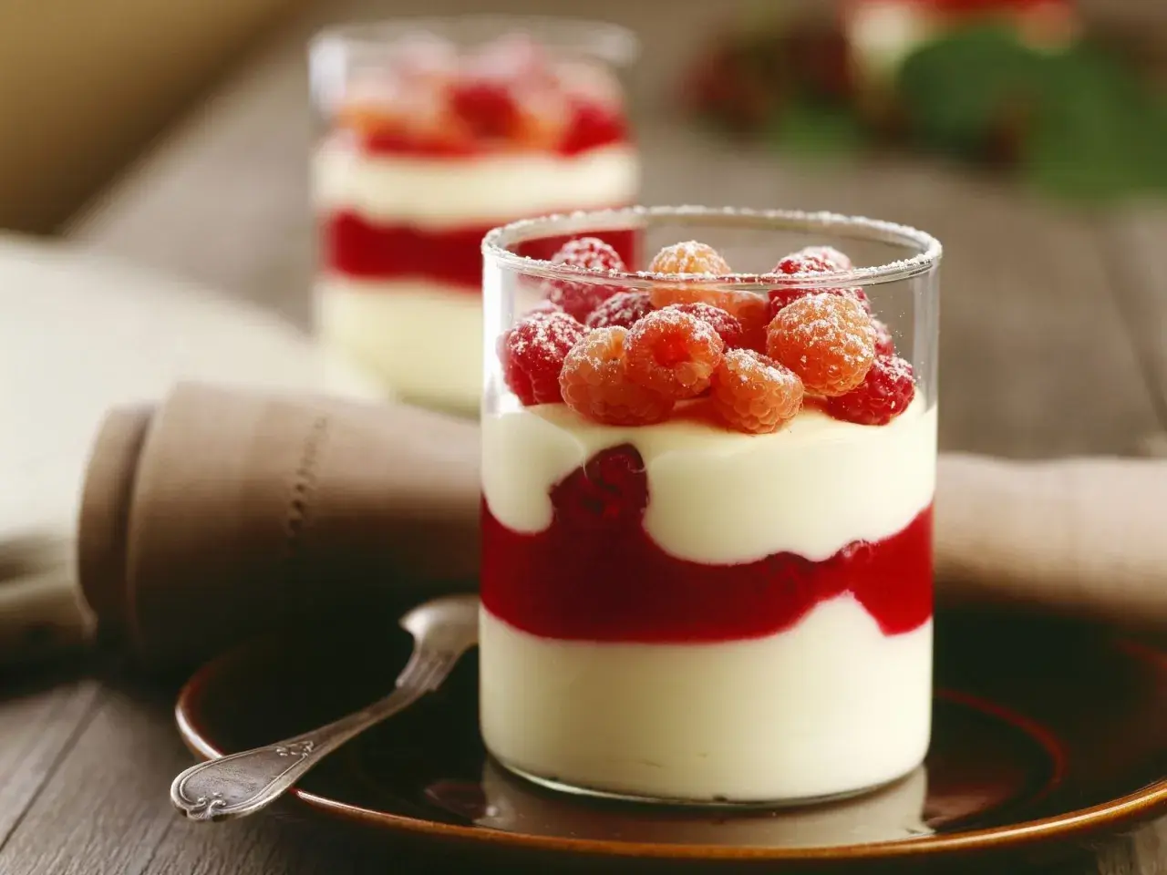 Zwei Gläser mit Schichten von Mousse au Chocolat Blanc, Himbeersauce und frischen Himbeeren, bestäubt mit Puderzucker.