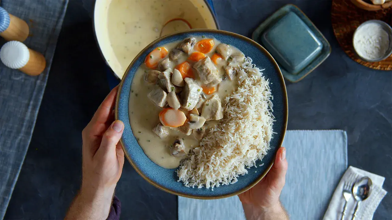 Ein Teller mit cremigem Blanquette de veau, Pilzen und Karotten, serviert mit Reis.