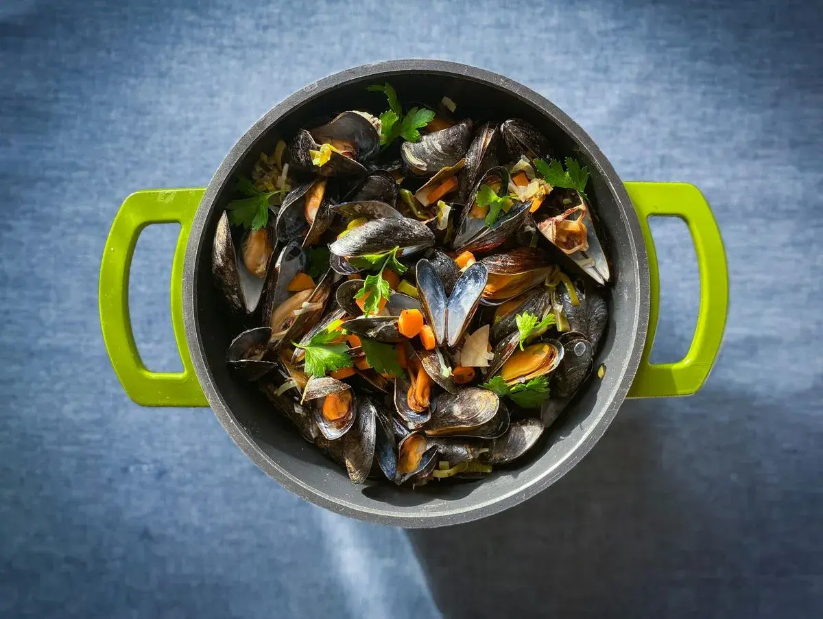 Ein Topf voller dampfender Moules Marinière, garniert mit frischer Petersilie und Karottenstücken, bereit zum Genuss.