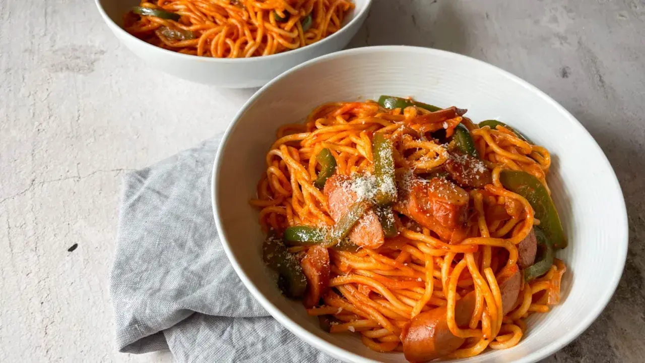 Zwei Schüsseln mit leckerem Spaghetti Napolitan, garniert mit Paprika und Wurst.