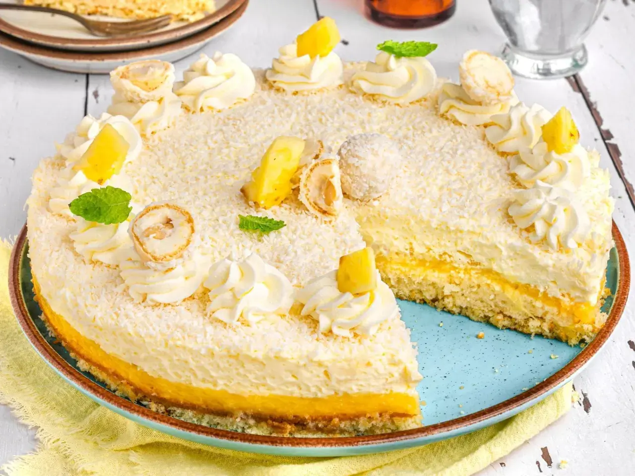 Ein köstlicher Ananas Kokos Kuchen, verziert mit Kokosraspeln, Sahnetuffs, Ananasstücken und Minze.