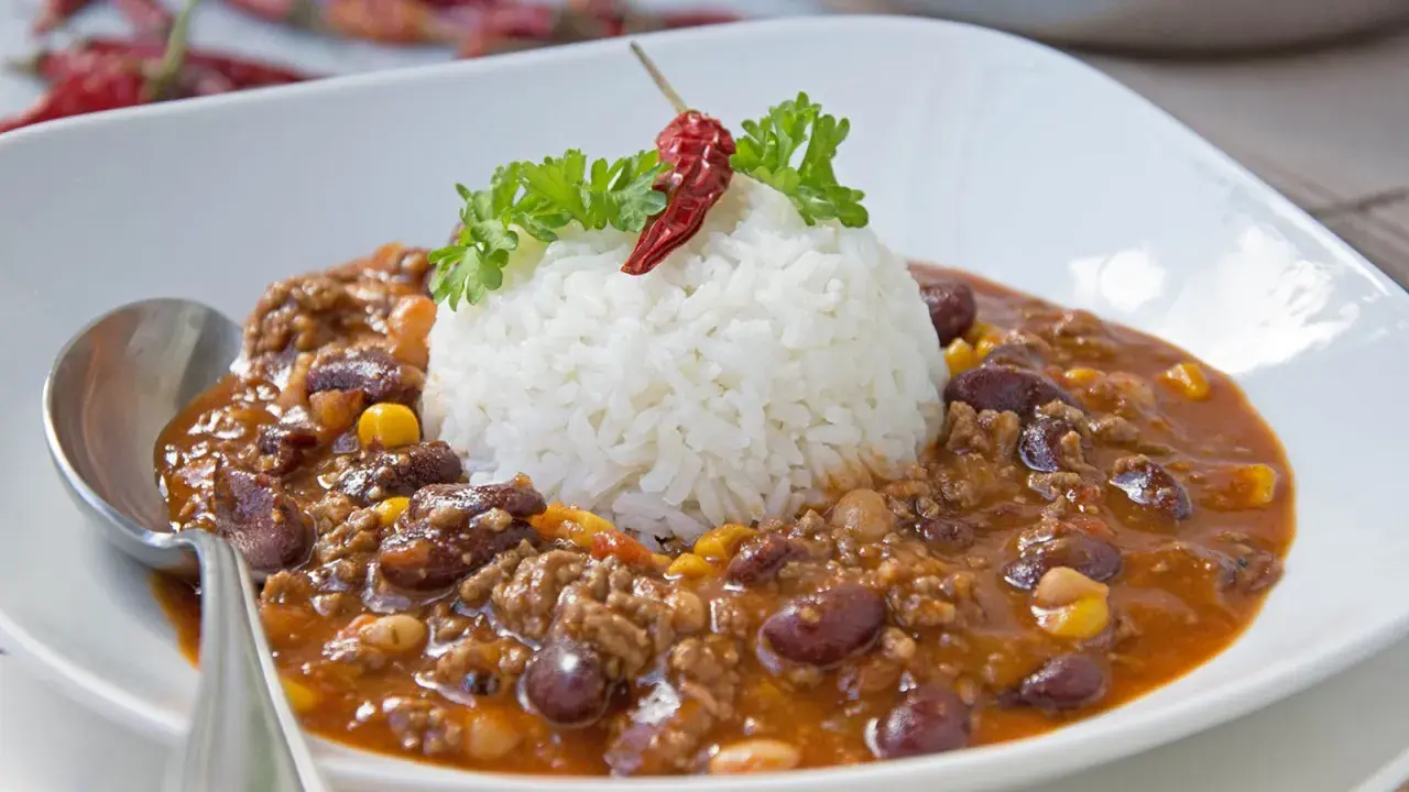 Herzhaftes Chili con Carne mit Reis, garniert mit Petersilie und einer getrockneten Chili.