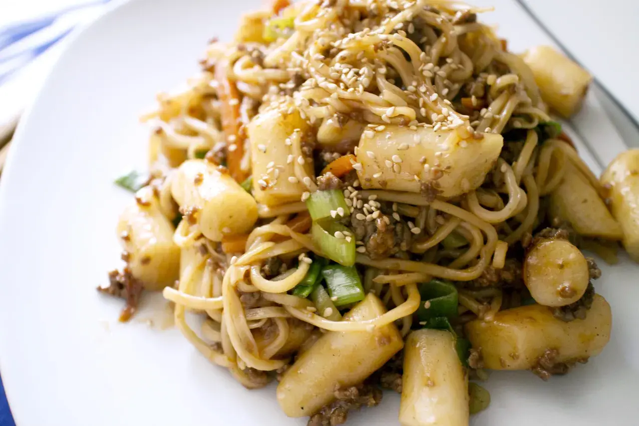 Yaki soba mit Hackfleisch, Möhren, Frühlingszwiebeln und Tteok (Reiskuchen), bestreut mit Sesam.