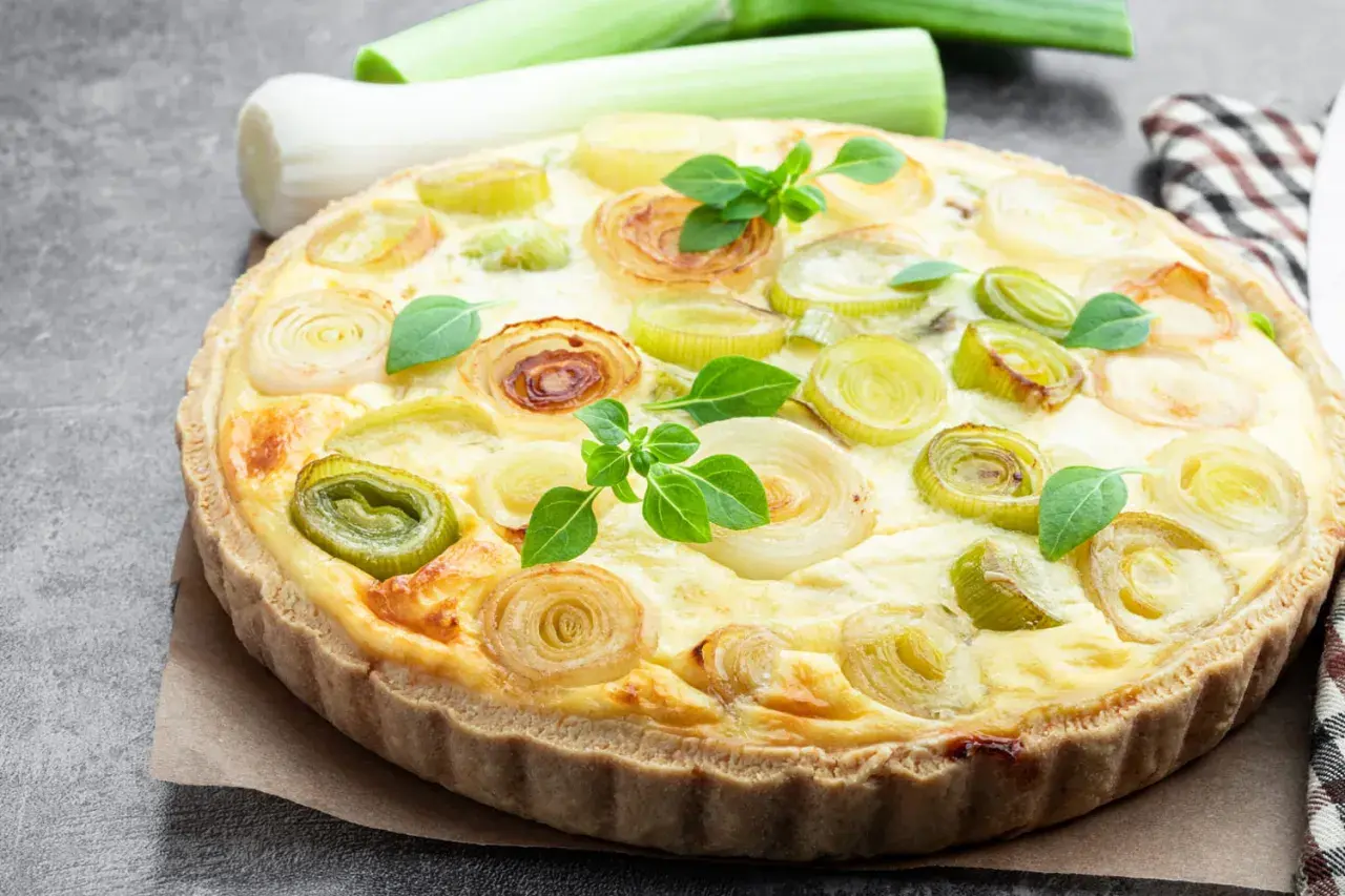 Herzhafte Quiche aux poireaux mit goldbraunem Teig und frischen Lauchringen, garniert mit grünen Kräutern.