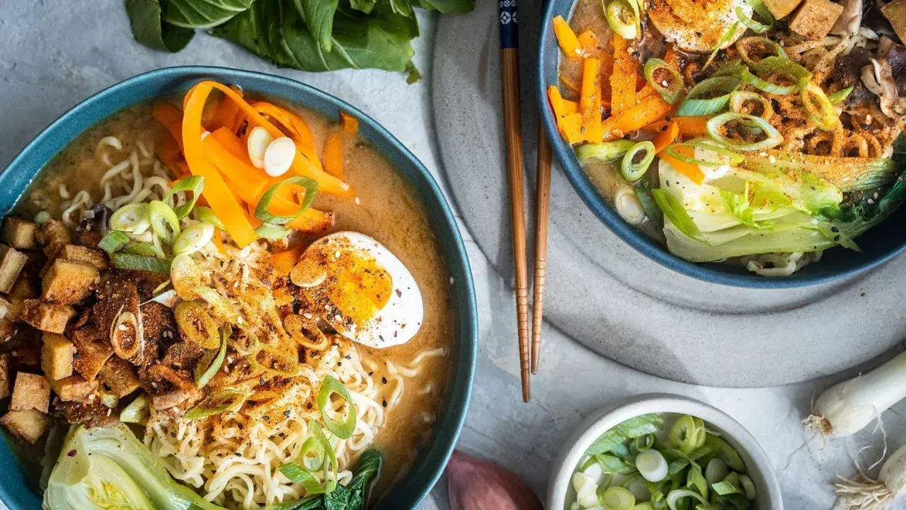 Zwei Schalen mit dampfendem, **vegetarischem Ramen**. Nudeln, Karottenstreifen, Pak Choi, Tofuwürfel und ein halbes Ei in herzhafter Brühe.