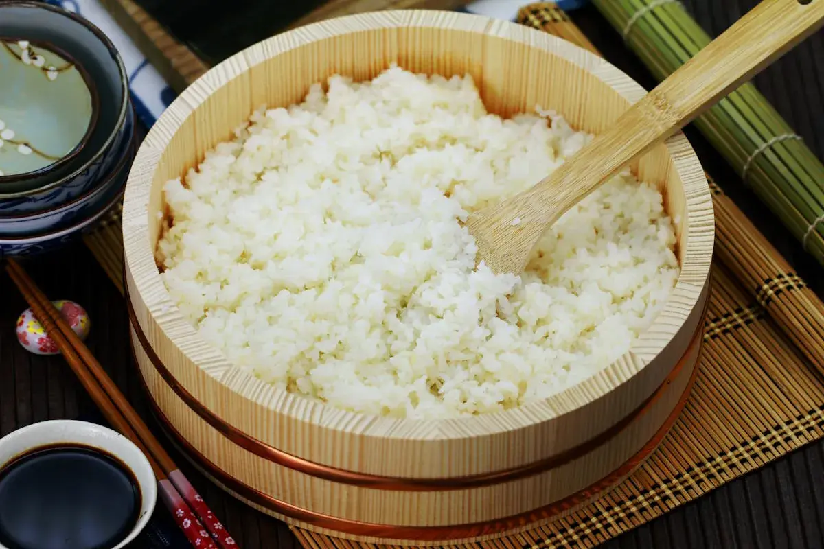 Perfekt zubereiteter sushi reis in einem hölzernen Behälter, bereit für die Zubereitung von Sushi. Daneben liegen Stäbchen und Sojasauce.