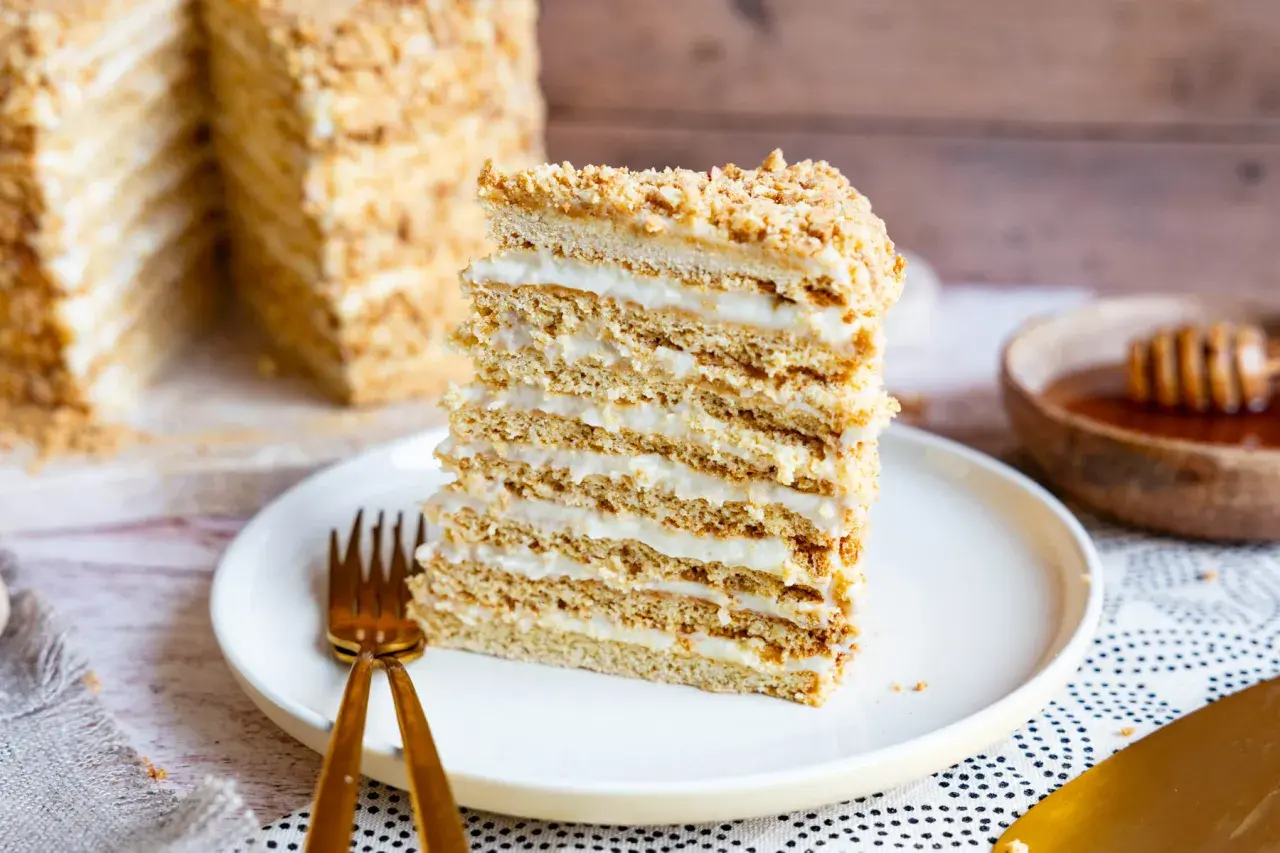 Ein Stück russischer Kuchen, geschichtet mit Honig und Sahne, auf einem Teller mit goldenem Besteck.