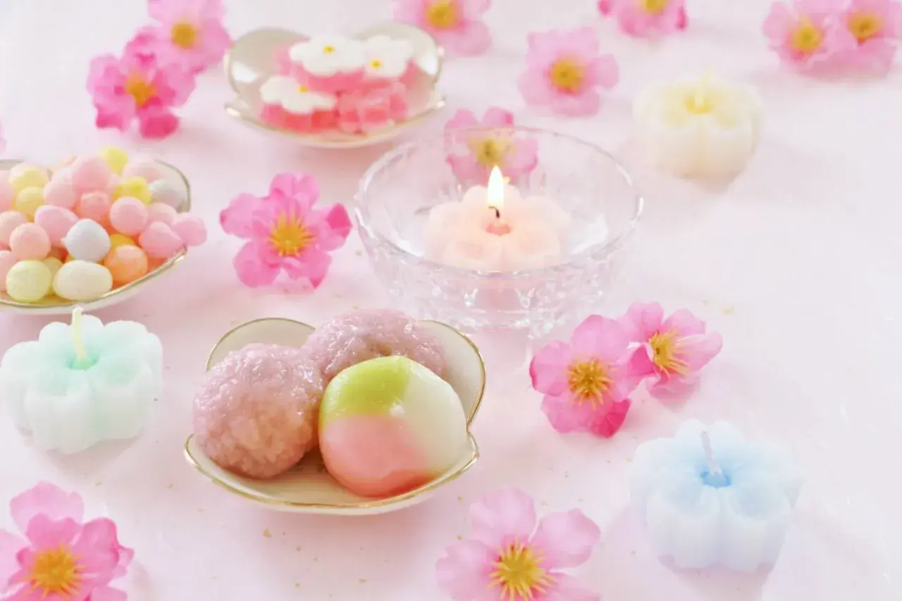 Zarte japanische Desserts, bunte Süßigkeiten und blütenförmige Kerzen auf rosa Untergrund.