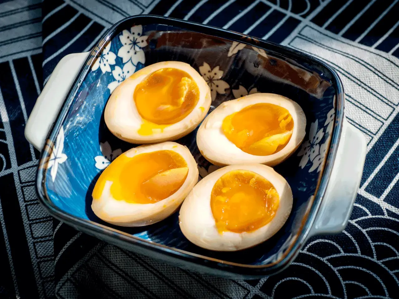Vier halbe, perfekt gekochte ramen eier mit flüssigem Eigelb in einer blauen Schale mit Kirschblütenmuster.