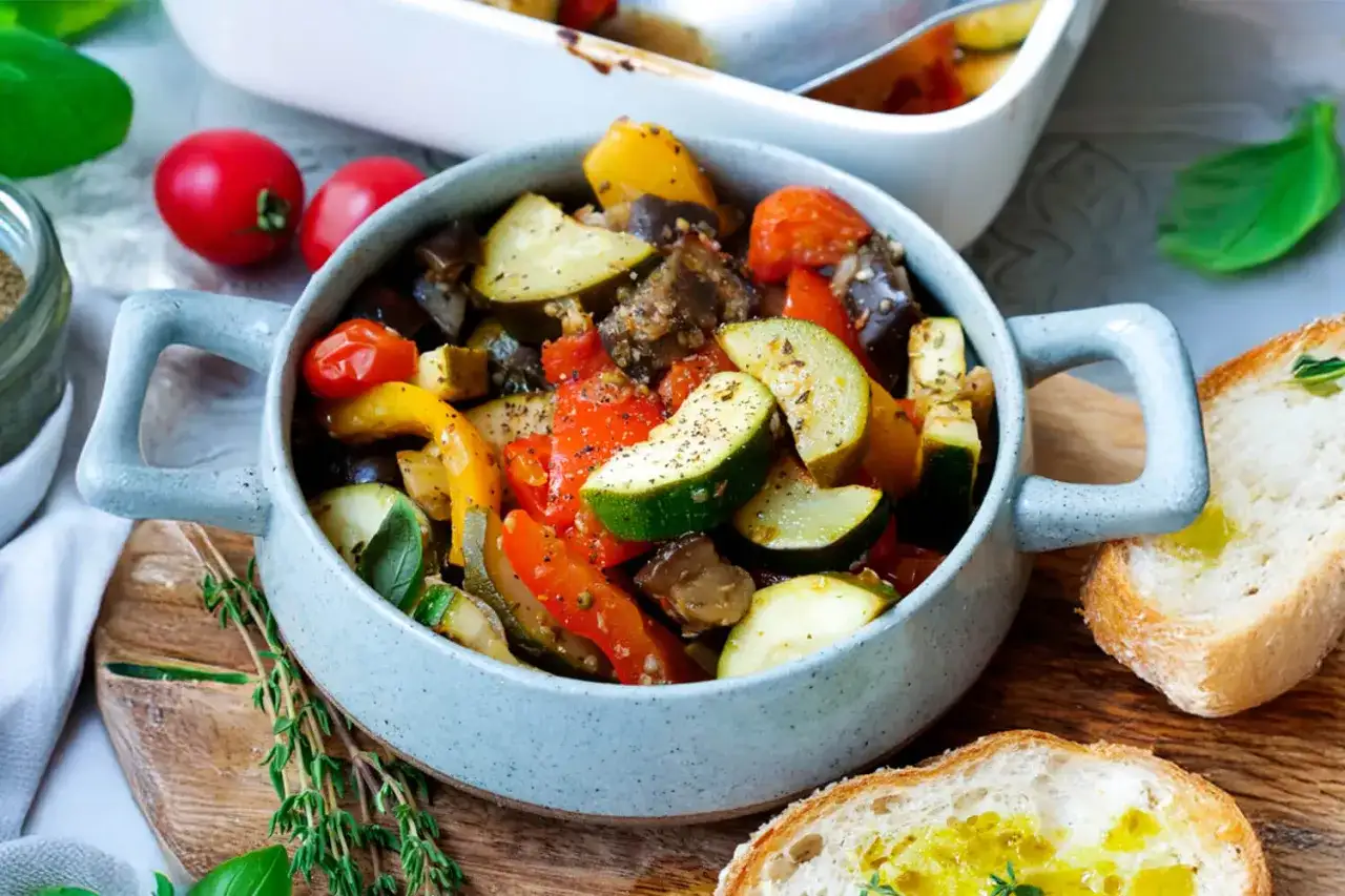Ein köstliches Ratatouille Rezept, serviert in einer grauen Schüssel, mit Zucchini, Paprika, Auberginen und Tomaten. Dazu knuspriges Brot.