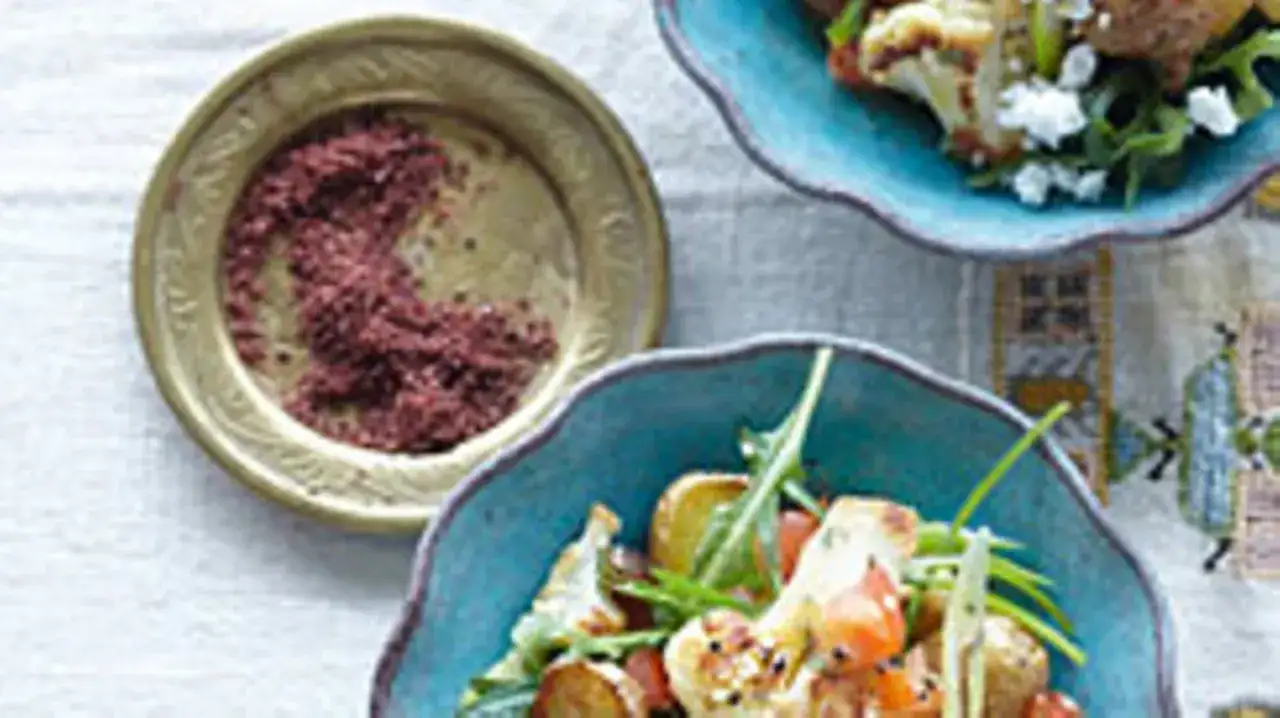 Gewürzschale mit rotem Pulver, vielleicht eine Sumach-Alternative, neben einem bunten Salat mit Blumenkohl und Ziegenkäse.