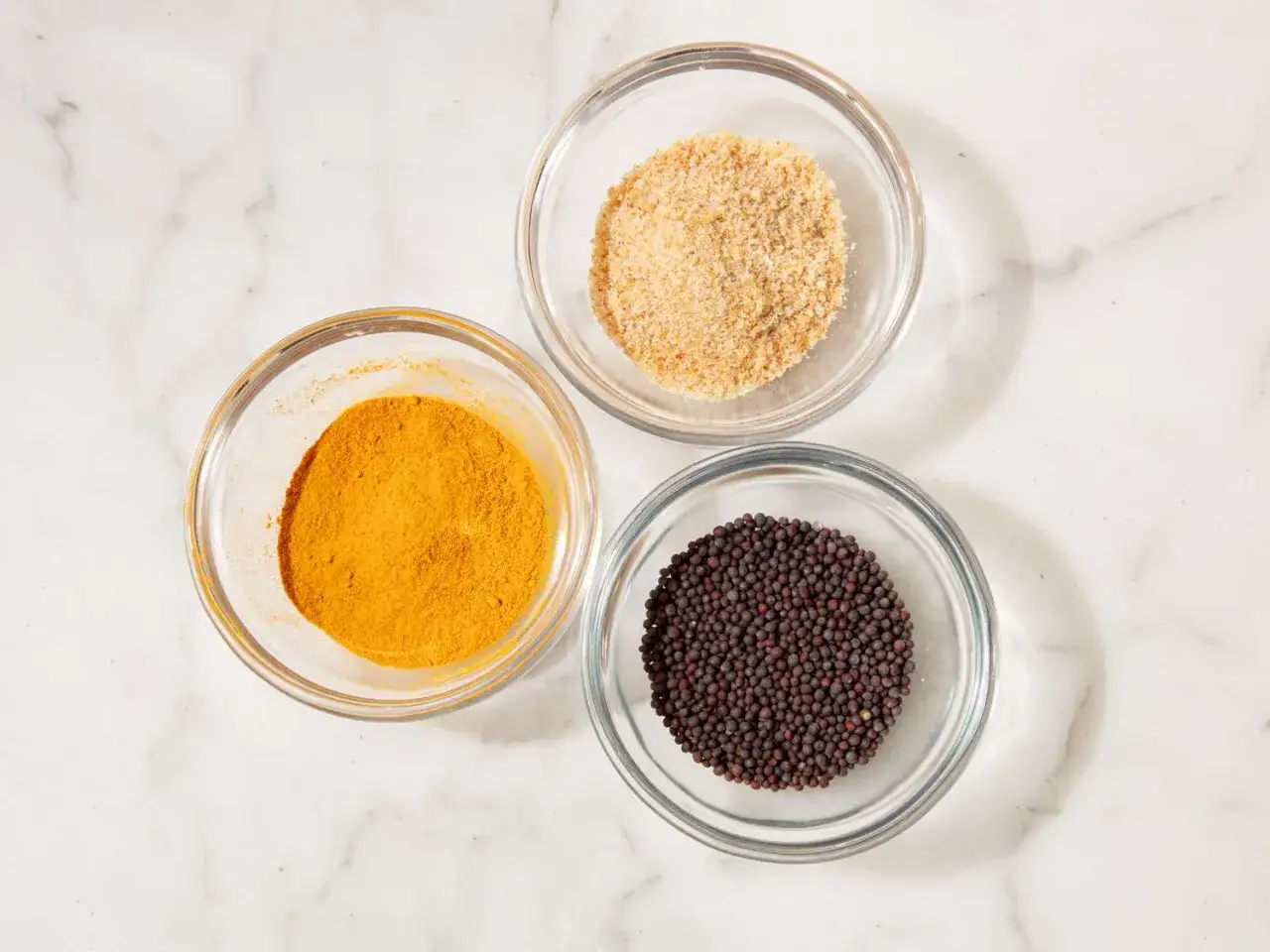 Drei Schalen mit Gew&uuml;rzen: Kurkumapulver, Senfk&ouml;rner und gemahlene Gew&uuml;rze. Sie sind Zutaten f&uuml;r Garam Masala.