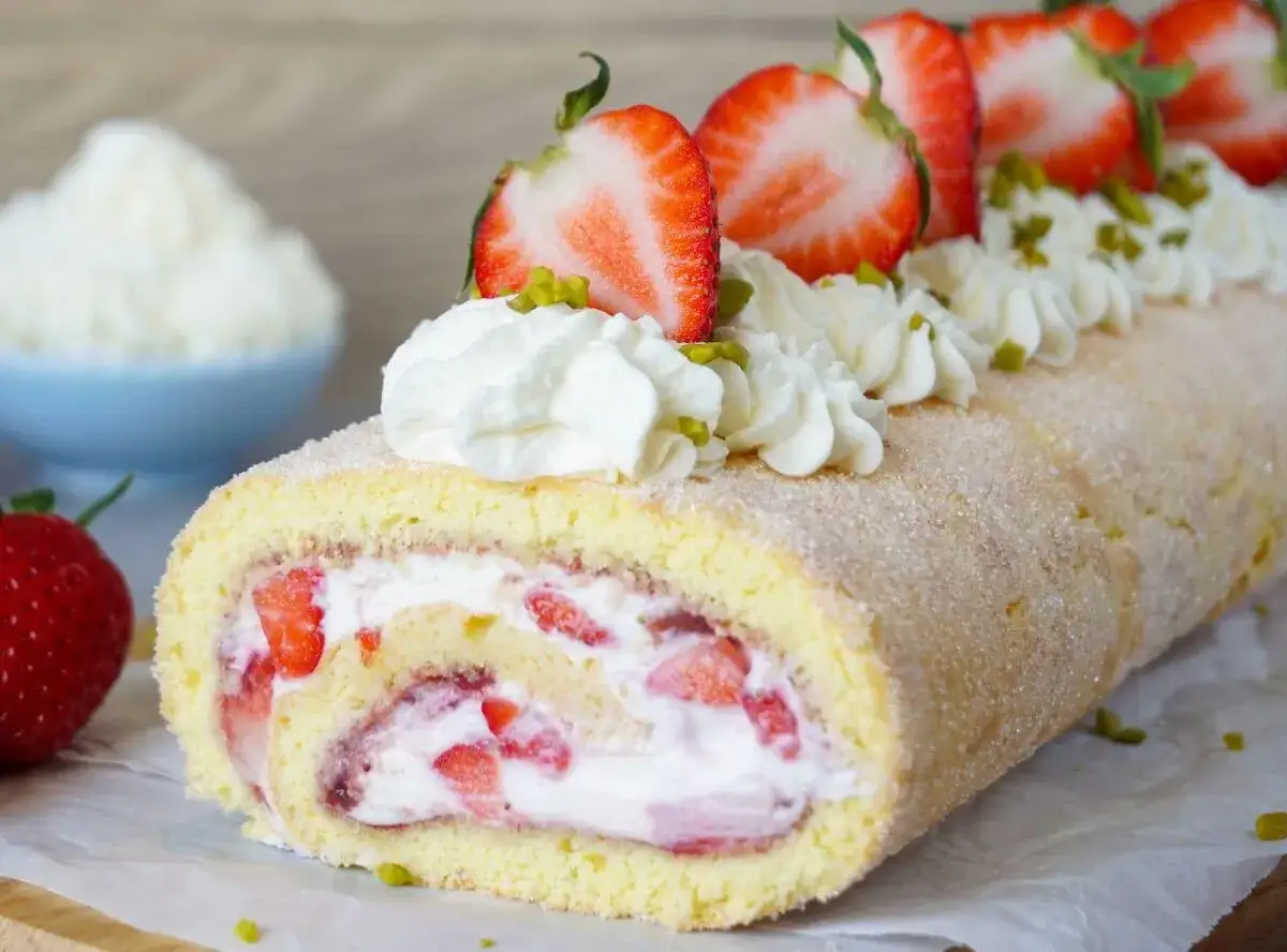 Ein k&ouml;stlicher Brazo de Reina, gef&uuml;llt mit Sahne und Erdbeeren, garniert mit frischen Erdbeerscheiben und Pistazien.