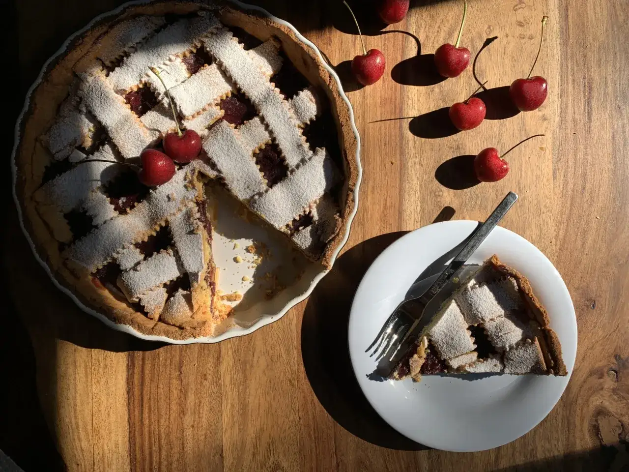 Ein köstliches Kirschkuchen-Rezept, das mit Puderzucker bestäubt ist. Frische Kirschen liegen daneben.