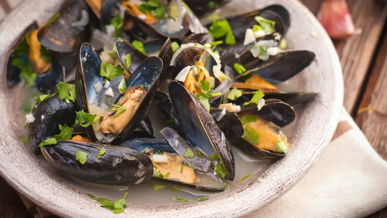 Ein Teller Moules Marinières, dampfend und mit frischer Petersilie garniert, bereit zum Genießen.