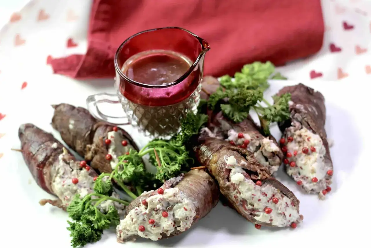 Rouladen gef&uuml;llt mit einer cremigen Masse, verziert mit roten Pfefferbeeren und Petersilie. Daneben ein kleiner Krug mit So&szlig;e.