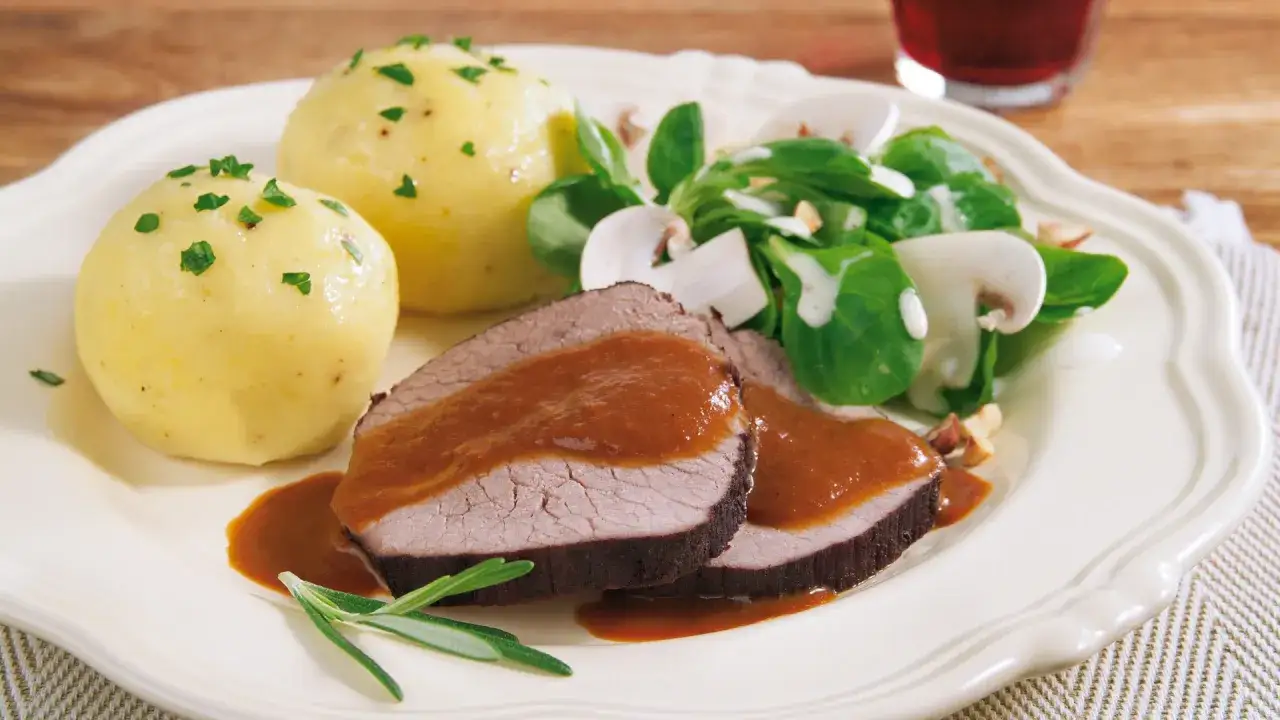 Boeuf à la mode: zarte Rindfleischscheiben mit Sauce, Kartoffelknödeln und einem frischen Salat mit Pilzen.
