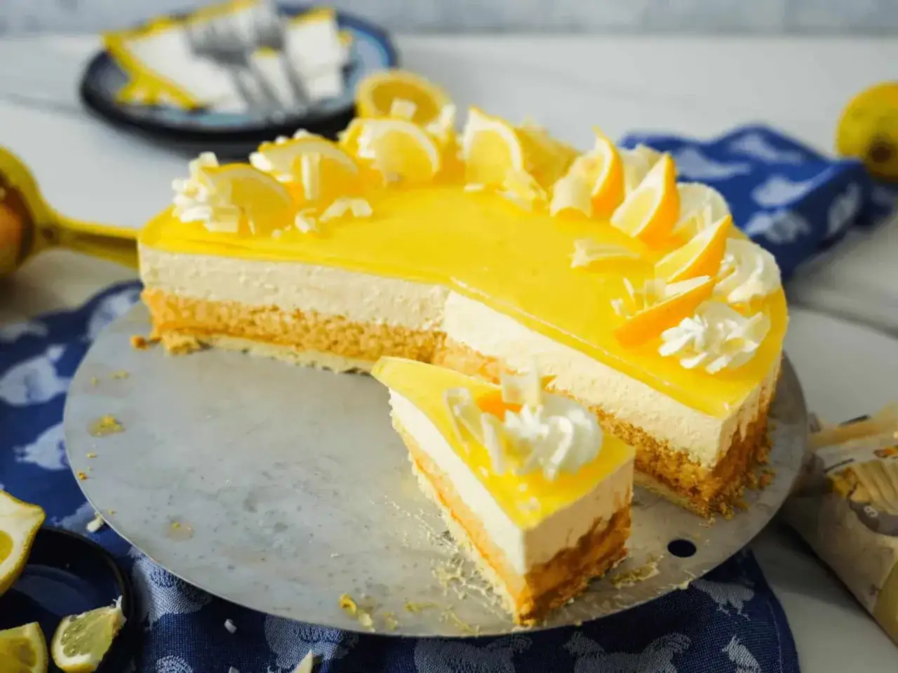 Süße Torte mit leuchtend gelber Glasur, dekoriert mit Zitronenscheiben und Sahnetupfern. Ein Stück mit cremigem Lemon Curd wartet darauf, genossen zu werden.