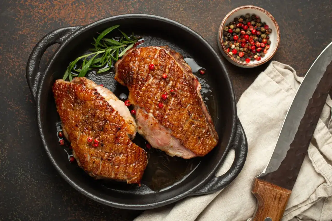 Zwei perfekt gebratene Entenbrustfilets in einer Pfanne, garniert mit Rosmarin und rosa Pfeffer. Ein köstliches Entenfilet Rezept, bereit zum Servieren.