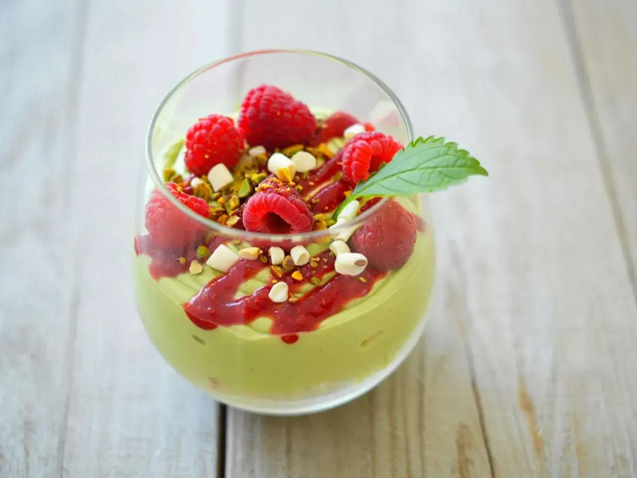 Cremiges Pistazienmousse im Glas, garniert mit frischen Himbeeren, gehackten Pistazien und einem Hauch Himbeersauce.
