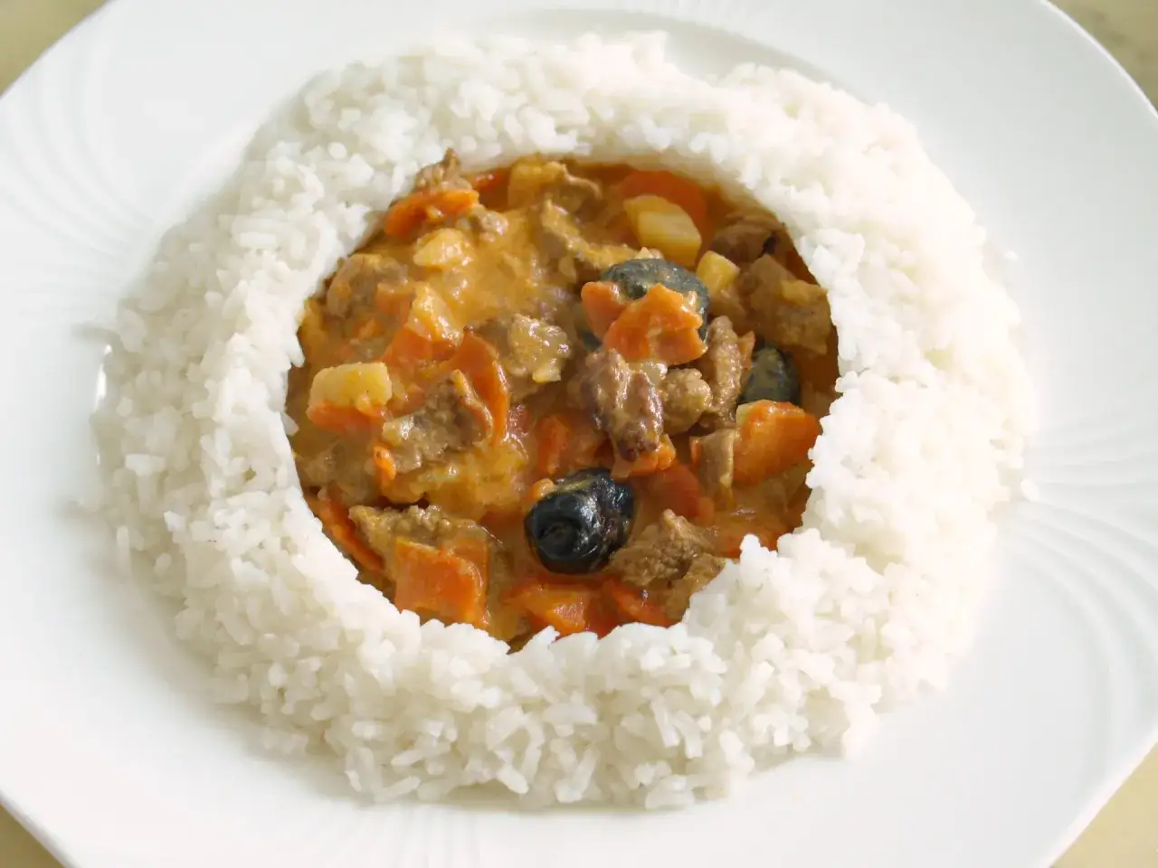 Ein Teller mit Blanquette de veau, einem cremigen Kalbfleischeintopf mit Karotten und Kartoffeln, umgeben von lockerem Reis.
