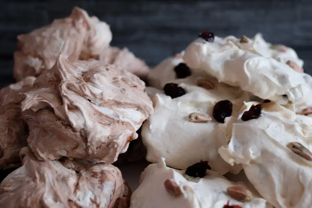 Zwei Stapel Baiser nach dem Backen: braun-wei&szlig;e und wei&szlig;e mit Cranberries und Pistazien. Sie sehen leicht klebrig aus.