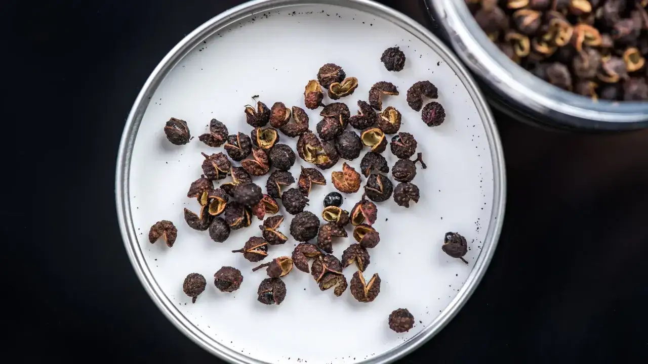 Ein Haufen Szechuanpfeffer-Beeren auf einer wei&szlig;en Oberfl&auml;che. Die kleinen, dunkelroten Beeren sind teilweise ge&ouml;ffnet und enth&uuml;llen ihr Inneres.