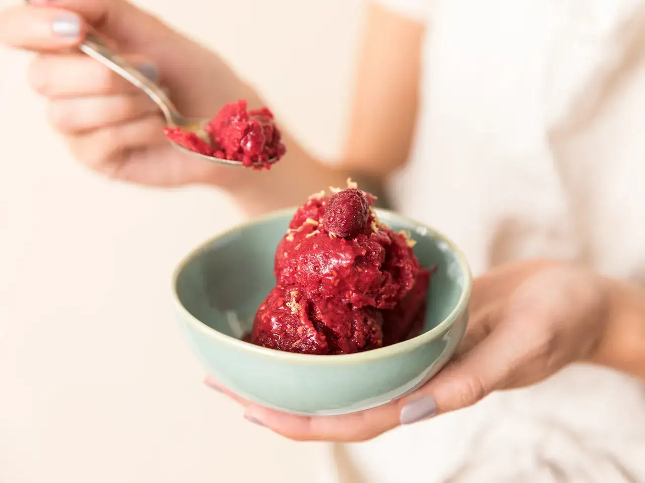 Eine L&ouml;ffelspitze voll Himbeersorbet wird aus einer Sch&uuml;ssel mit dem leuchtend roten, gefrorenen Dessert gehoben.