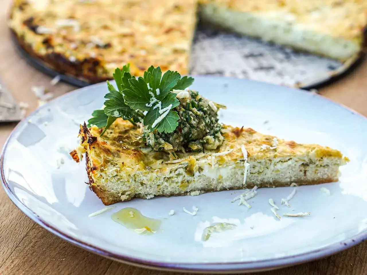 Ein St&uuml;ck Quiche aux poireaux mit Kr&auml;utertopping und Petersilie auf einem Teller.