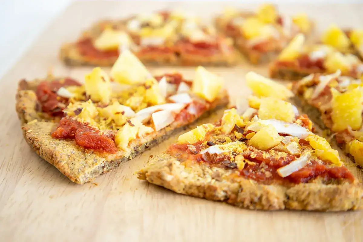 Vegane Blumenkohl Pizza mit Ananas und Tomatensauce, auf einem Holzbrett serviert.