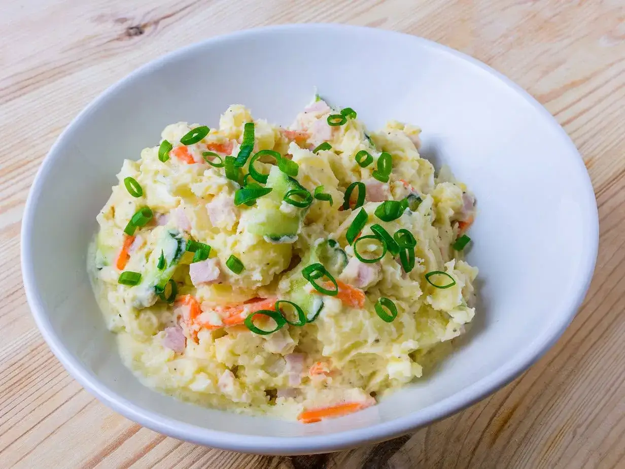 Cremiger japanischer Kartoffelsalat mit Karotten, Gurken und Fr&uuml;hlingszwiebeln in einer wei&szlig;en Sch&uuml;ssel.