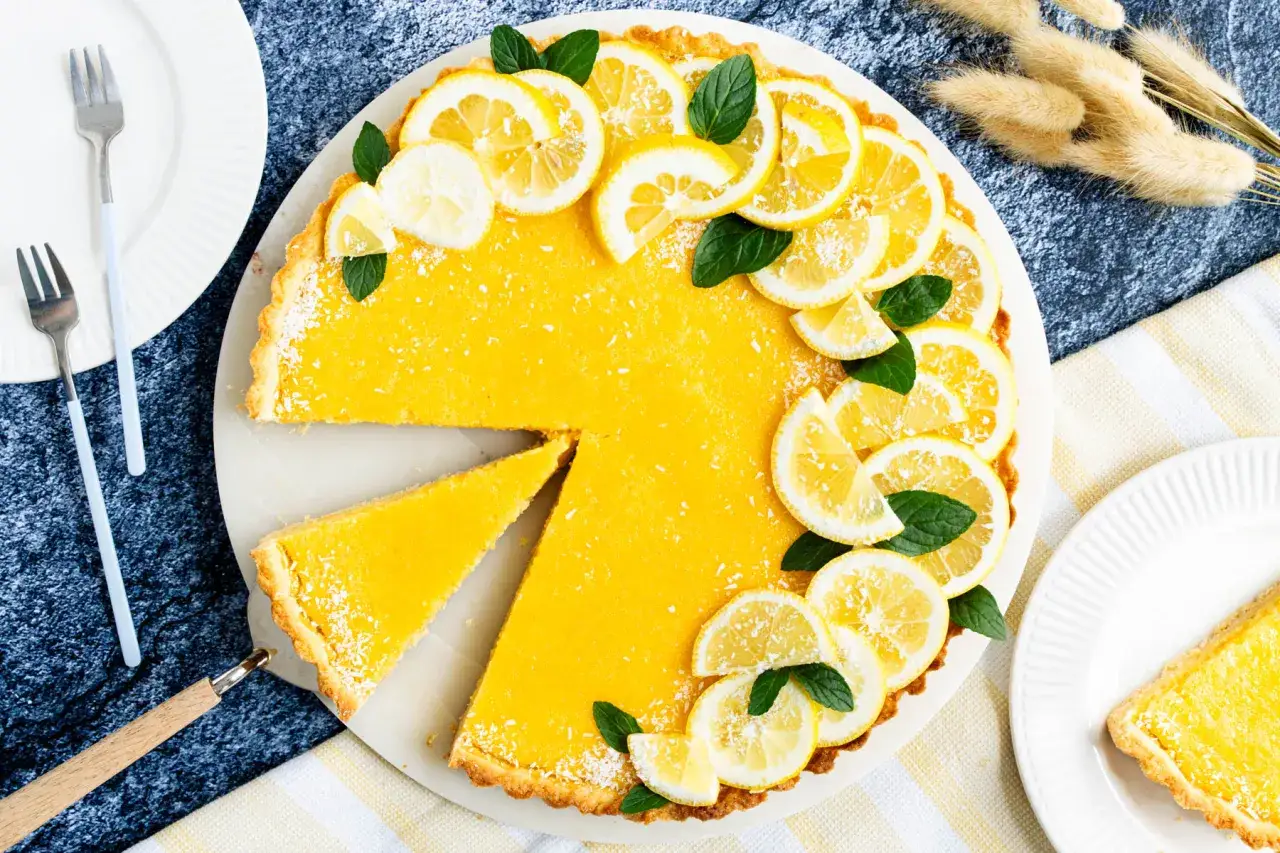 Eine leuchtend gelbe Tarte au Citron, garniert mit Zitronenscheiben und Minze, wartet darauf, angeschnitten zu werden.