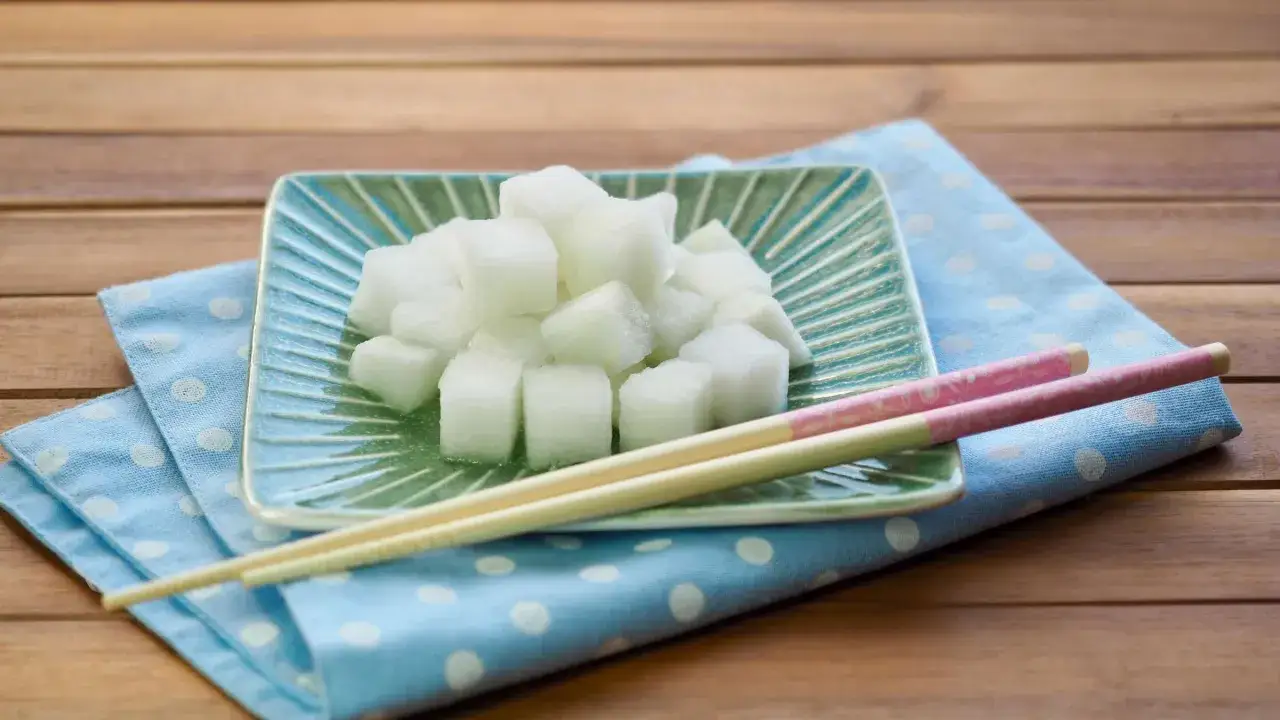 W&uuml;rfel von daikon rettich auf einem gr&uuml;nen Teller, daneben St&auml;bchen auf einem blauen Tupftuch.