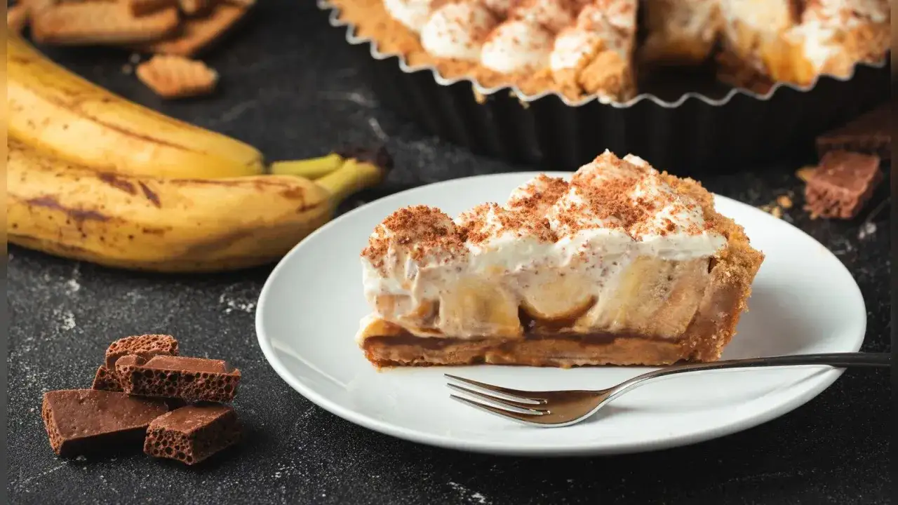 Ein St&uuml;ck Banoffee Pie mit Bananen, Karamell und Sahne, bestreut mit Schokoraspeln. Perfekt f&uuml;r ein Banoffee Pie Rezept.
